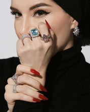 Close-up of  Viv Halil wearing multiple VH rings with gemstones on a plain background