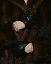 Close-up of model's black gloves embellished with VH moissanite tennis bracelets and fur coat