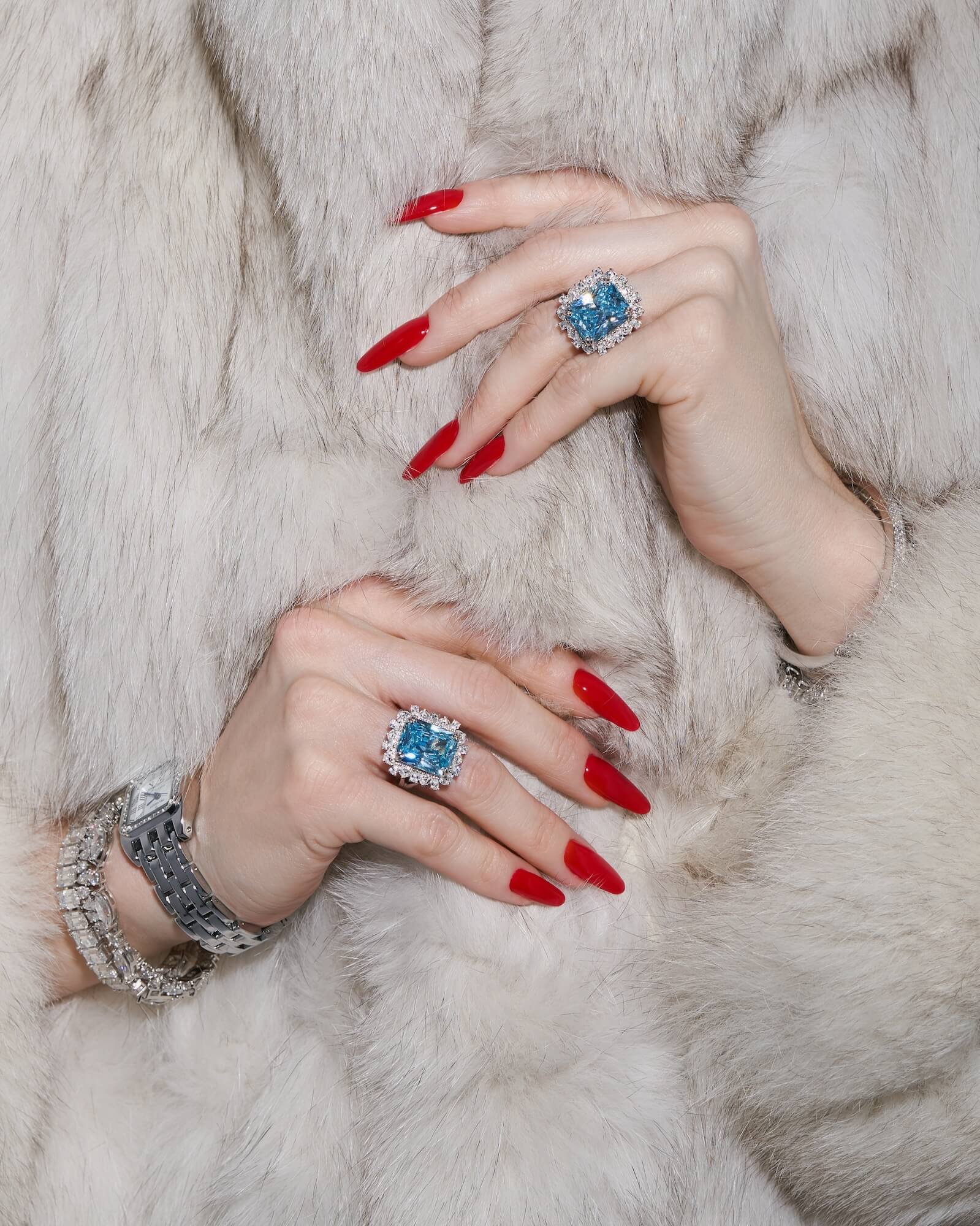 Close-up of model's hands wearing the Sissi statement cocktail ring with a sky blue emerald-cut zirconia center stone and halo cluster in sterling silver