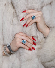 Close-up of model's hands wearing the Sissi statement cocktail ring with a sky blue emerald-cut zirconia center stone and halo cluster in sterling silver