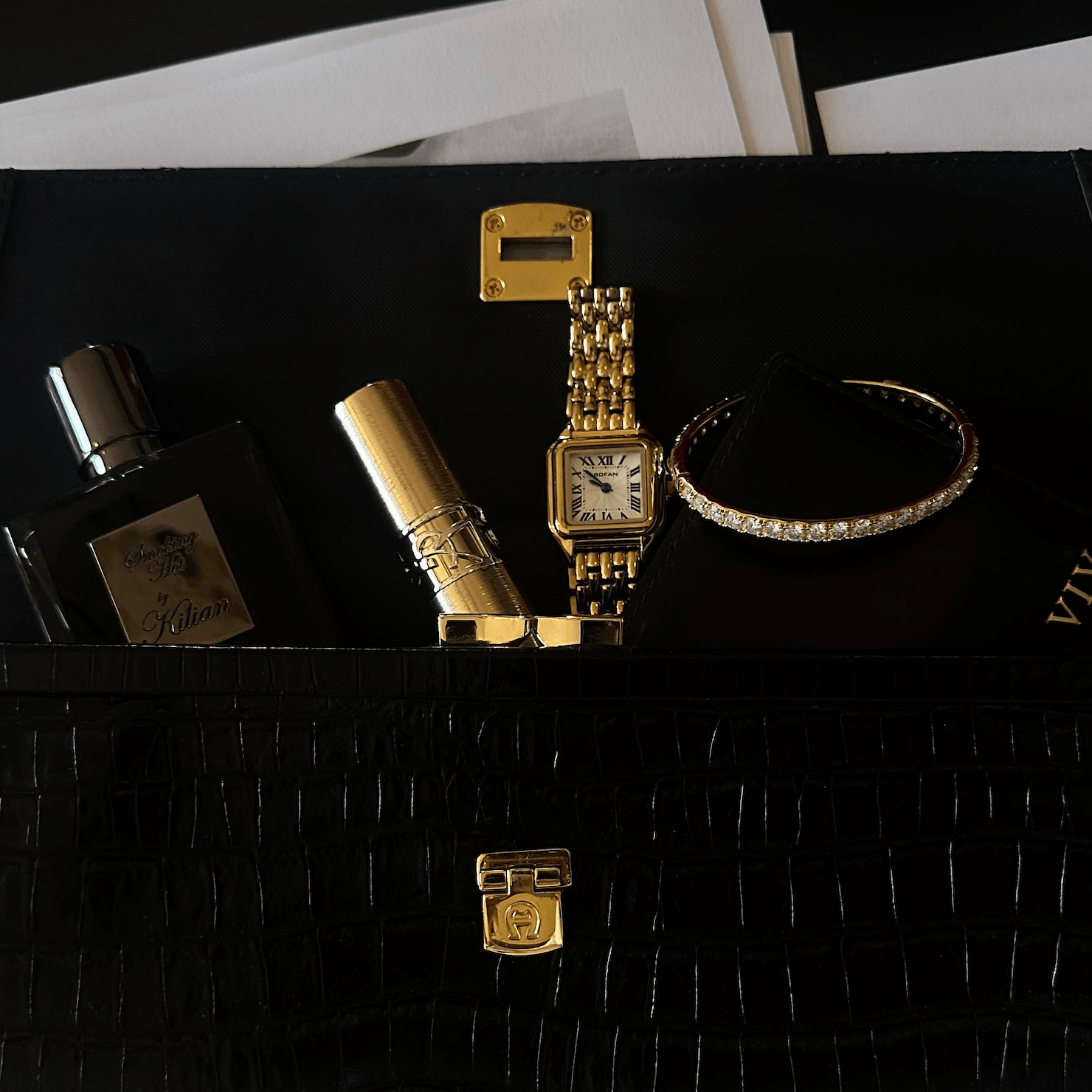 Designer black handbag containing a Cartier watch, the Eternity Moissanite Bangle Bracelet, lipstick and perfume bottle.