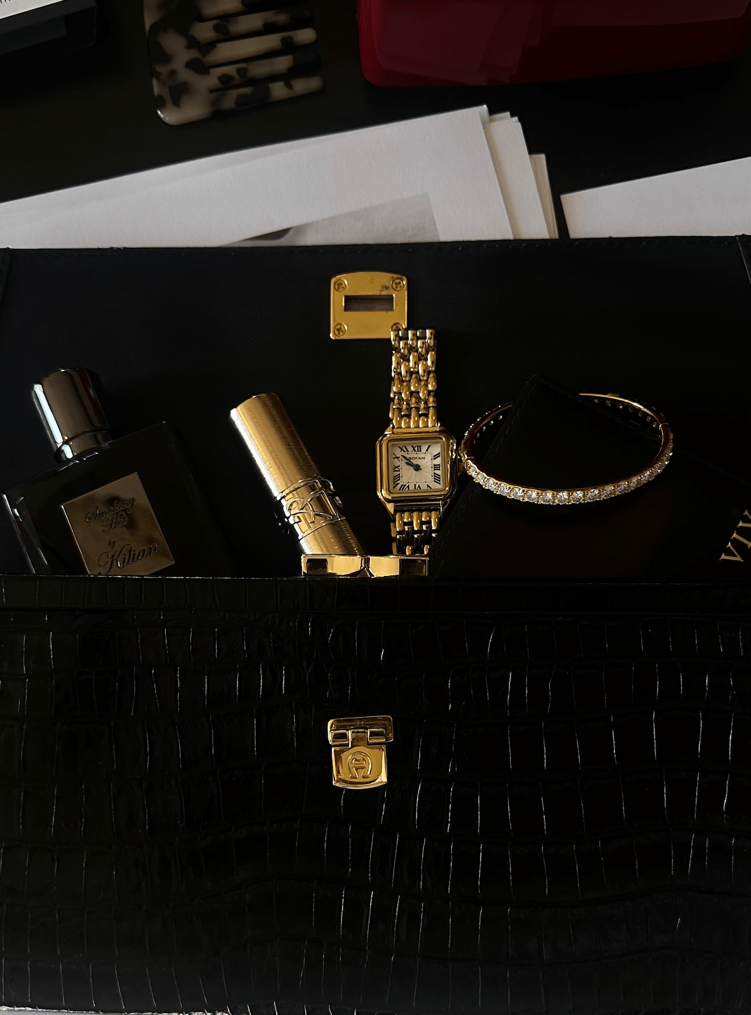Designer black handbag containing a Cartier watch, the Eternity Moissanite Bangle Bracelet, lipstick and perfume bottle.