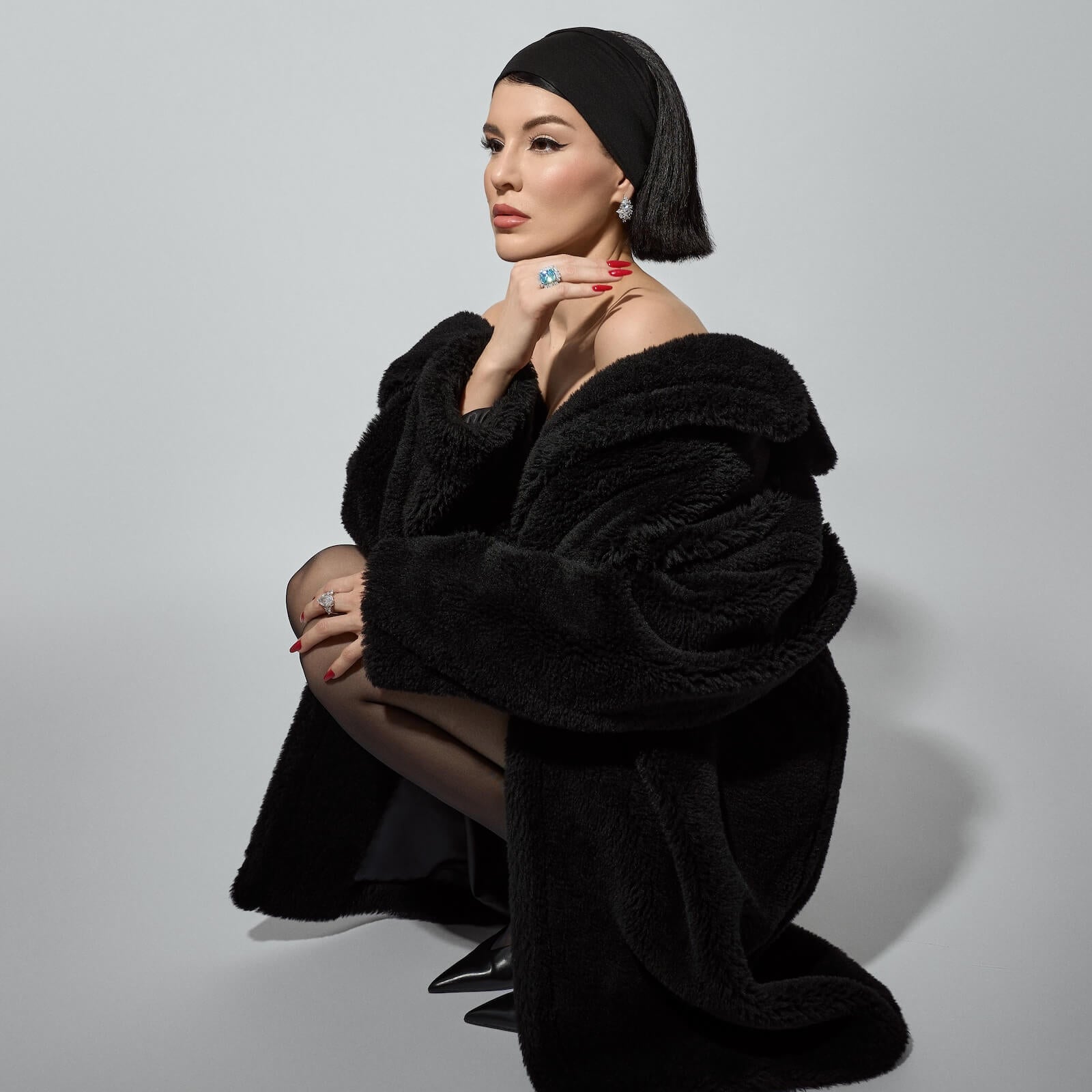 Viv Halil wearing a black fur coat and headscarf on a gray background