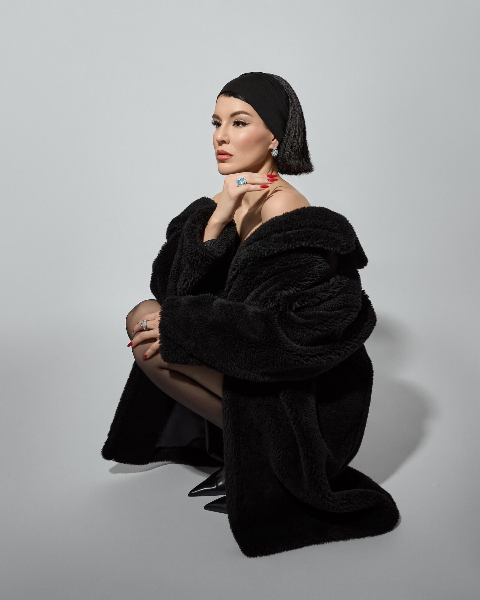 Viv Halil wearing a black fur coat and headscarf on a gray background