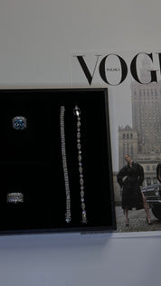 VH earrings are displayed on a black jewelry box along with moissanite tennis bracelets with a Vogue magazine in the background.
