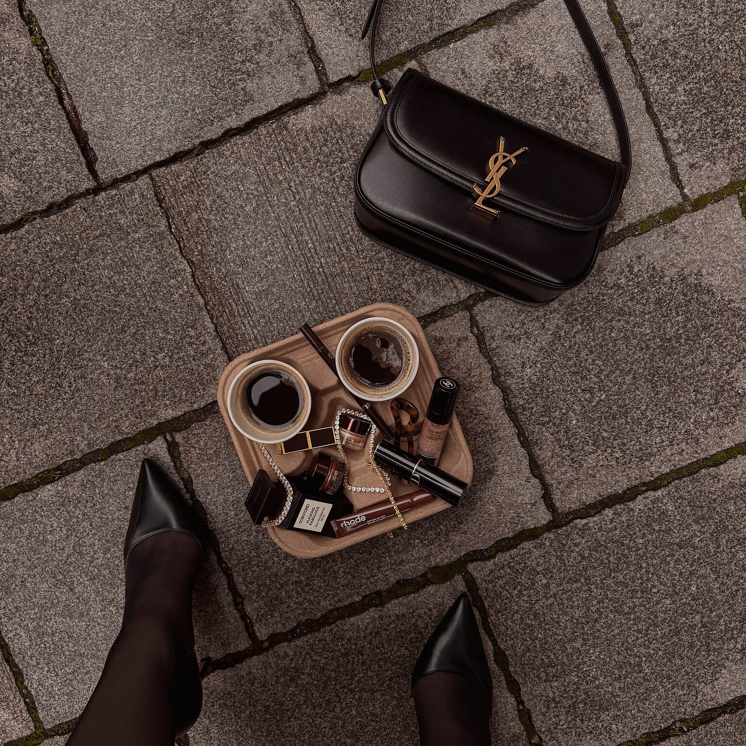 Black YSL handbag on a stone pavement with a tray of coffee and a variety of VH jewelry.