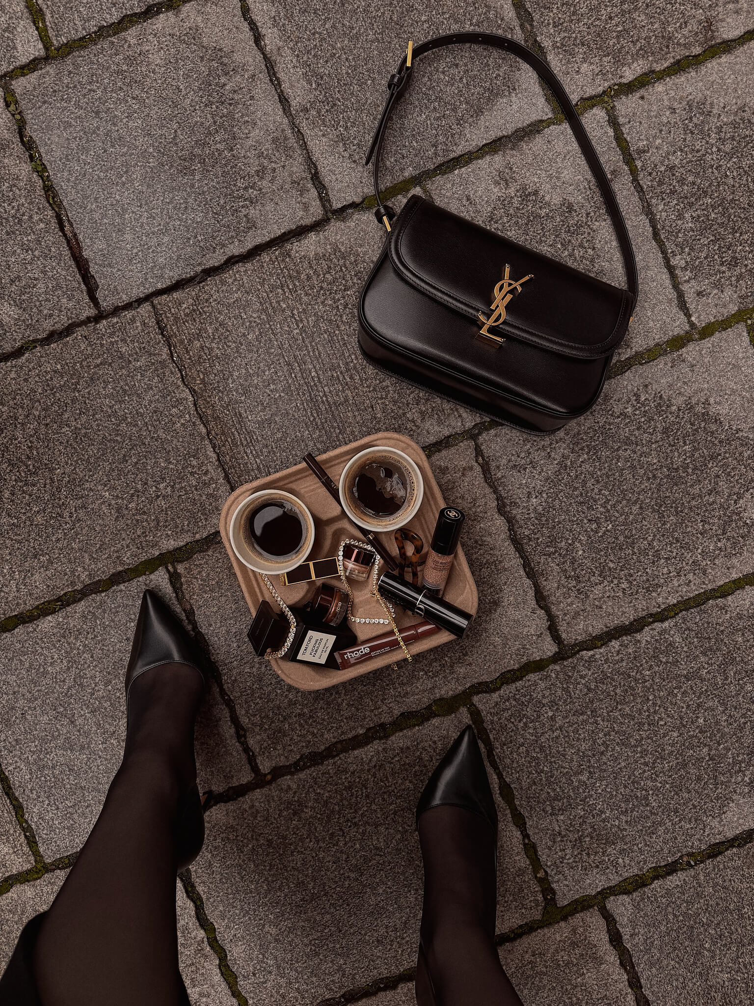 Black YSL handbag on a stone pavement with a tray of coffee and a variety of VH jewelry.
