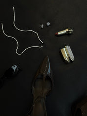Black surface with high-heeled shoes, lipsticks, sunglasses, the Nazari tennis necklace and the Louis double halo cluster earrings.
