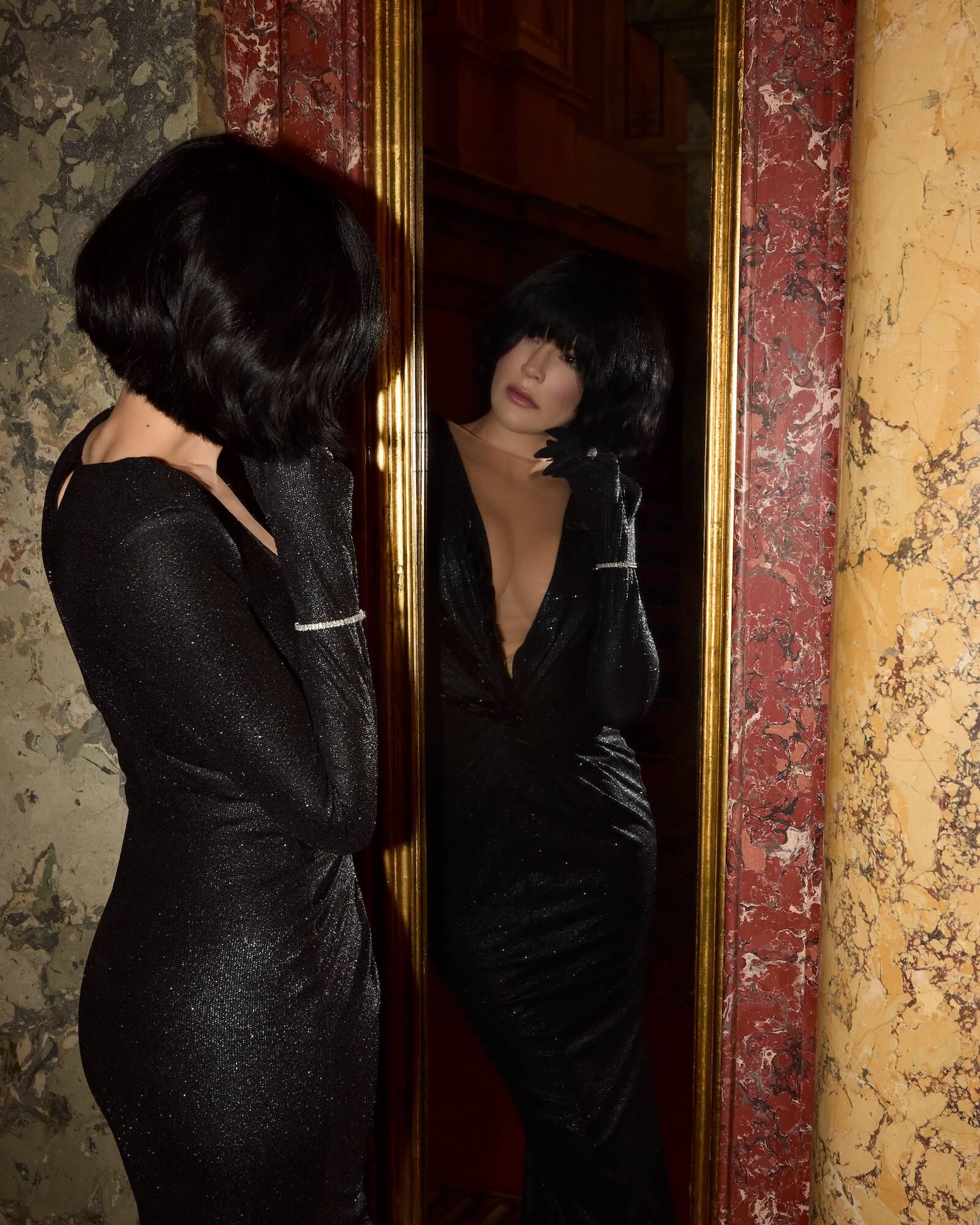 Luxury jewelry designer Viv Halil is in a black dress, looking at herself in a mirror with a decorative frame. Wearing the novi tennis bracelet. 