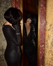 Luxury jewelry designer Viv Halil is in a black dress, looking at herself in a mirror with a decorative frame. Wearing the novi tennis bracelet. 
