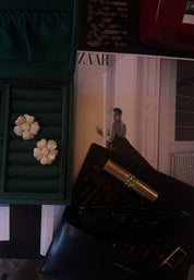 Flower-shaped earrings in a green jewelry box with a magazine and perfume bottle in the background.