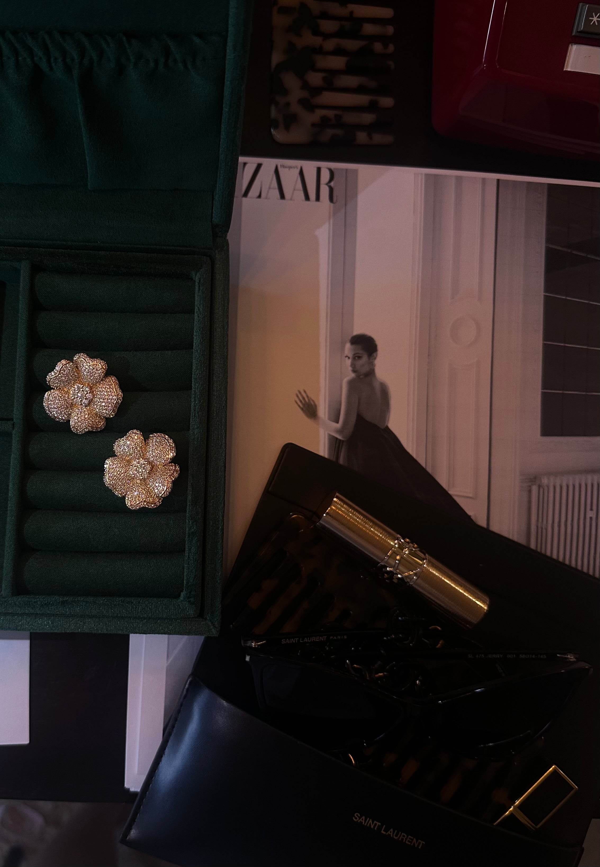 Flower-shaped earrings in a green jewelry box with a magazine and perfume bottle in the background.