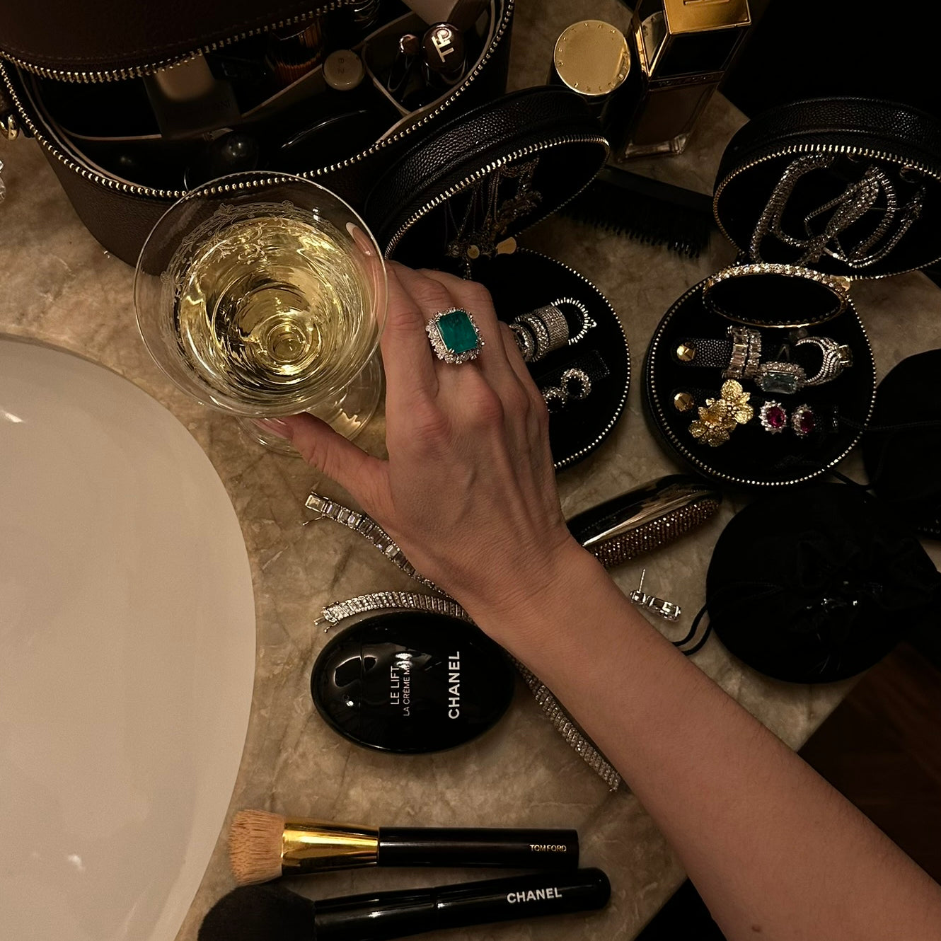 Viv Halil preparing for an evening out with makeup and a glass of wine on bathroom vanity displaying The Mini Travel Jewelry Box by Viviana Halil. 