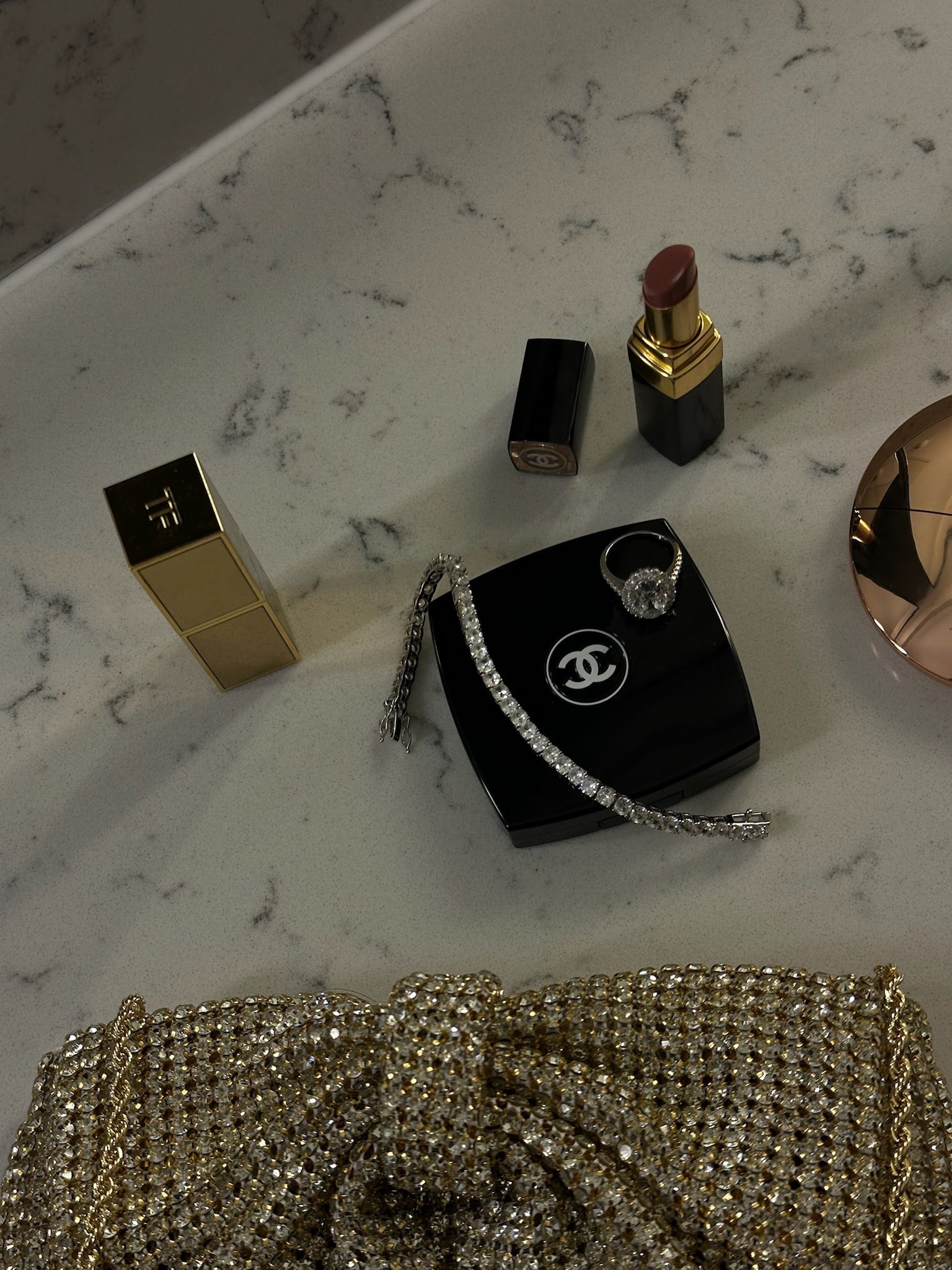 Makeup items including a lipstick and lip gloss on a marble surface with a Chanel handbag features The Mon Cheri Ring by Viviana Halil